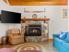 Ein Wohnzimmer mit Kamin aus Stein, einem an der Wand befestigten Fernseher und einem blauen Sofa mit dekorativem Kissen.
