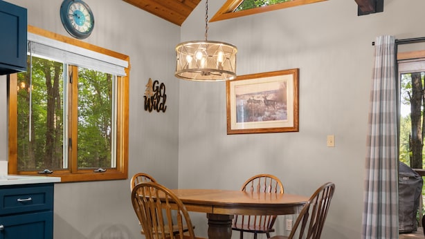 A dining area with a wooden table and chairs, a hanging light fixture, a clock, and a framed picture on the wall.