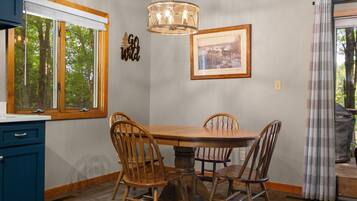 Un coin repas avec une table et des chaises en bois, un luminaire suspendu, une horloge et un tableau encadré au mur.