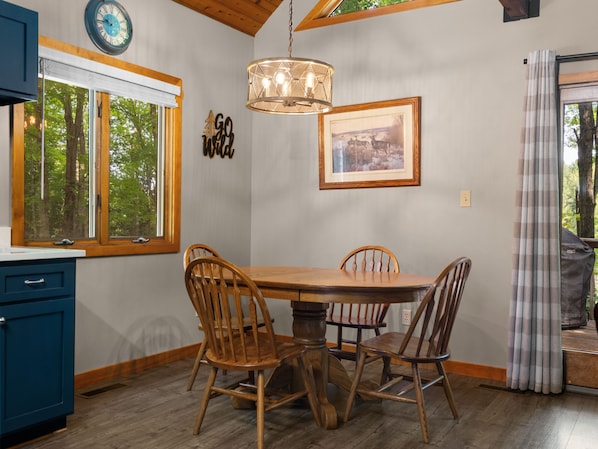 A dining area with a wooden table and chairs, a hanging light fixture, a clock, and a framed picture on the wall.