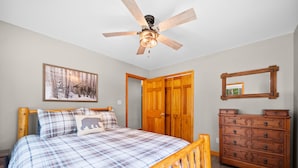 A bedroom with a wooden bed, a ceiling fan, a dresser, a mirror, and a framed picture on the wall.