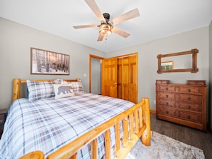 A bedroom with a wooden bed, a ceiling fan, a dresser, a mirror, and a framed picture on the wall.