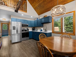 A modern kitchen with stainless steel appliances, blue cabinets, and a dining area with wooden furniture.