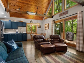 A spacious living area with a wooden ceiling, a fireplace, a dining table with chairs, and a view of the outdoors through large windows.