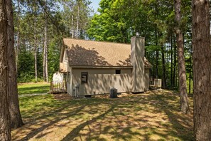 A single-story cabin with a chimney, surrounded by trees.