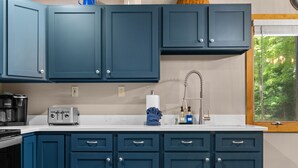A kitchen with dark blue cabinets, a white countertop, a toaster, a coffee maker, and a window with a view of trees.