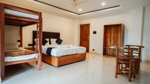 A bedroom with a bunk bed, a single bed, a desk with chairs, and a wardrobe. - Sayora Hotels (Port Blair)