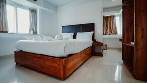 A modern bedroom with a wooden bed, a nightstand, and a wardrobe. - Sayora Hotels (Port Blair)