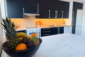 A kitchen with dark cabinets, a marble countertop, and a bowl of fruit. - Modern 4BR Beachfront Apartment with Dock + Free Parking (Rogaland)