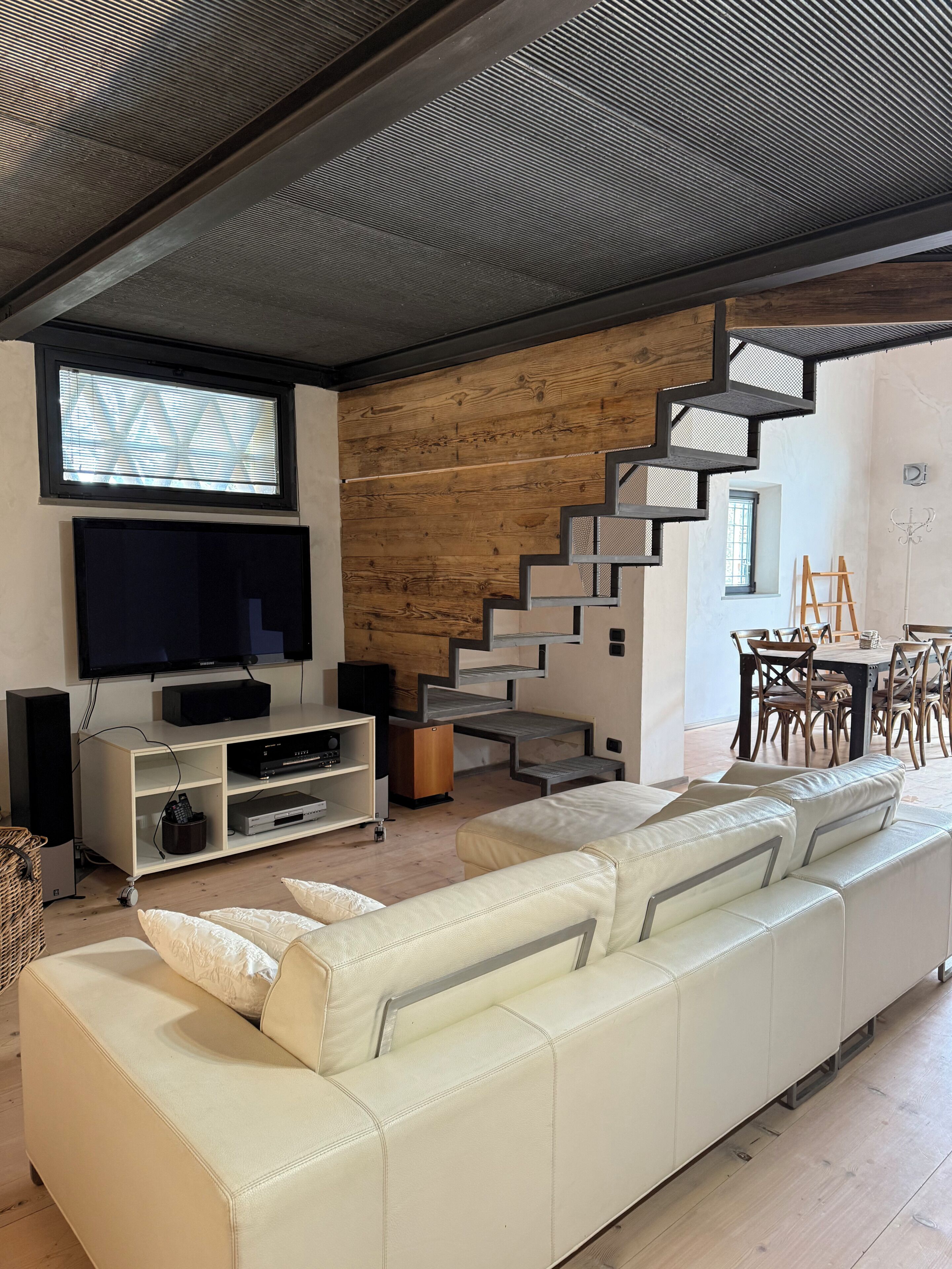 Un salon moderne avec un canapé blanc, un téléviseur à écran plat, un mur en bois et un escalier.