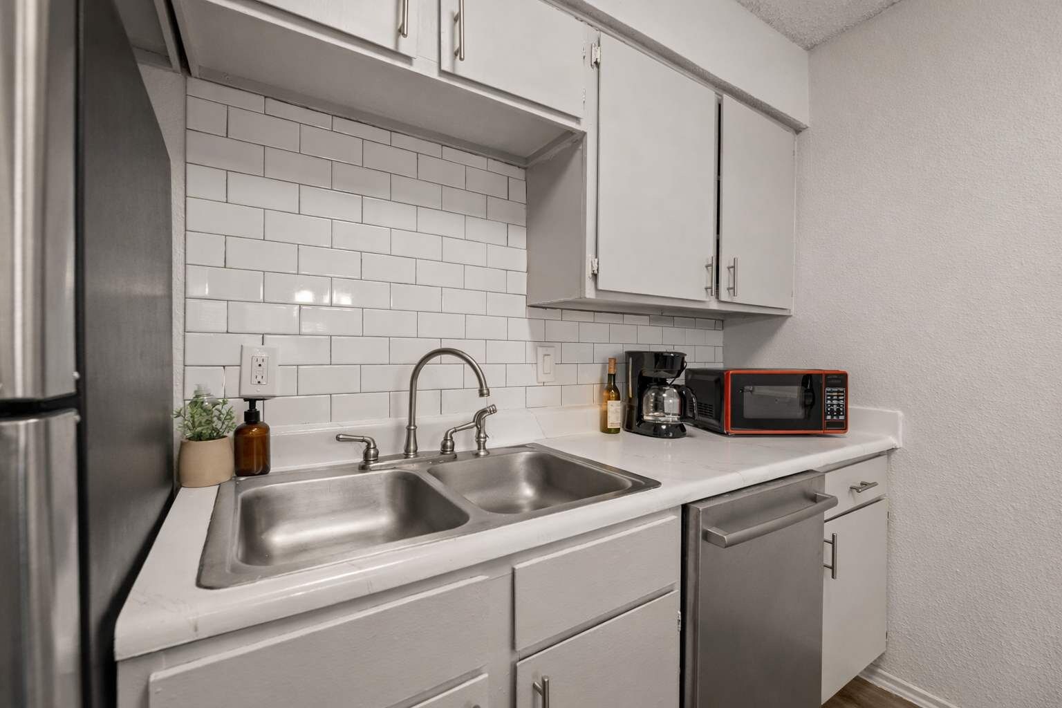 A modern kitchen with stainless steel appliances, white cabinetry, and a double sink.