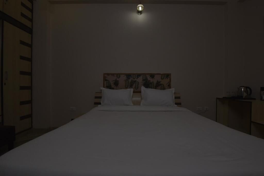 Una habitación de hotel tenuemente iluminada con una cama individual, un cabecero estampado con motivos florales y una mesita con una tetera.