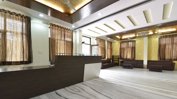A reception area with a marble floor, dark reception desk, brown curtains, and a seating area with sofas and a coffee table. - Hotel The Grand Kailash (Jaipur)