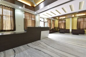 A reception area with a marble floor, dark reception desk, brown curtains, and a seating area with sofas and a coffee table. - Hotel The Grand Kailash (Jaipur)