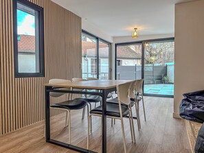 Ein moderner Essbereich mit Holztisch und -stühlen, großen Fenstern und Blick auf den Garten.