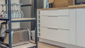 A modern kitchen with a stainless steel toaster, a glass shelf with wine glasses, white cabinets, and a wooden countertop. - #IM | The Victoria 10 💟 (Grenoble)