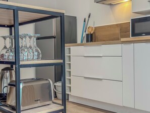 Una cocina moderna con un tostador de acero inoxidable, un estante de vidrio con copas de vino, armarios blancos y una encimera de madera.