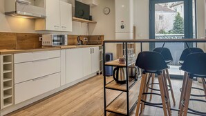 A modern kitchen with white cabinets, a microwave, and a coffee maker. There is a wooden counter and a small dining area with black chairs. - #IM | The Victoria 10 💟 (Grenoble)