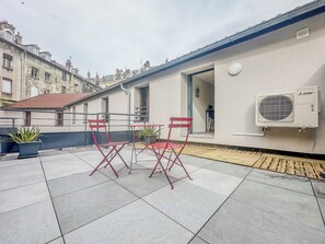 Una terraza en la azotea con dos sillas plegables rojas, una planta en maceta y un equipo de aire acondicionado Mitsubishi.
