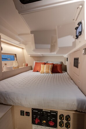 A bed with a control panel below it, a window with a view of the sea, and a small shelf with items. - Sun-Kissed Sailing Adventure in Islas Sarónicas (Piraeus)
