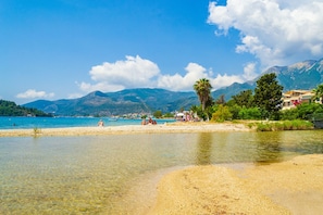 A beach with clear water, a sandy shore, and mountains in the background.