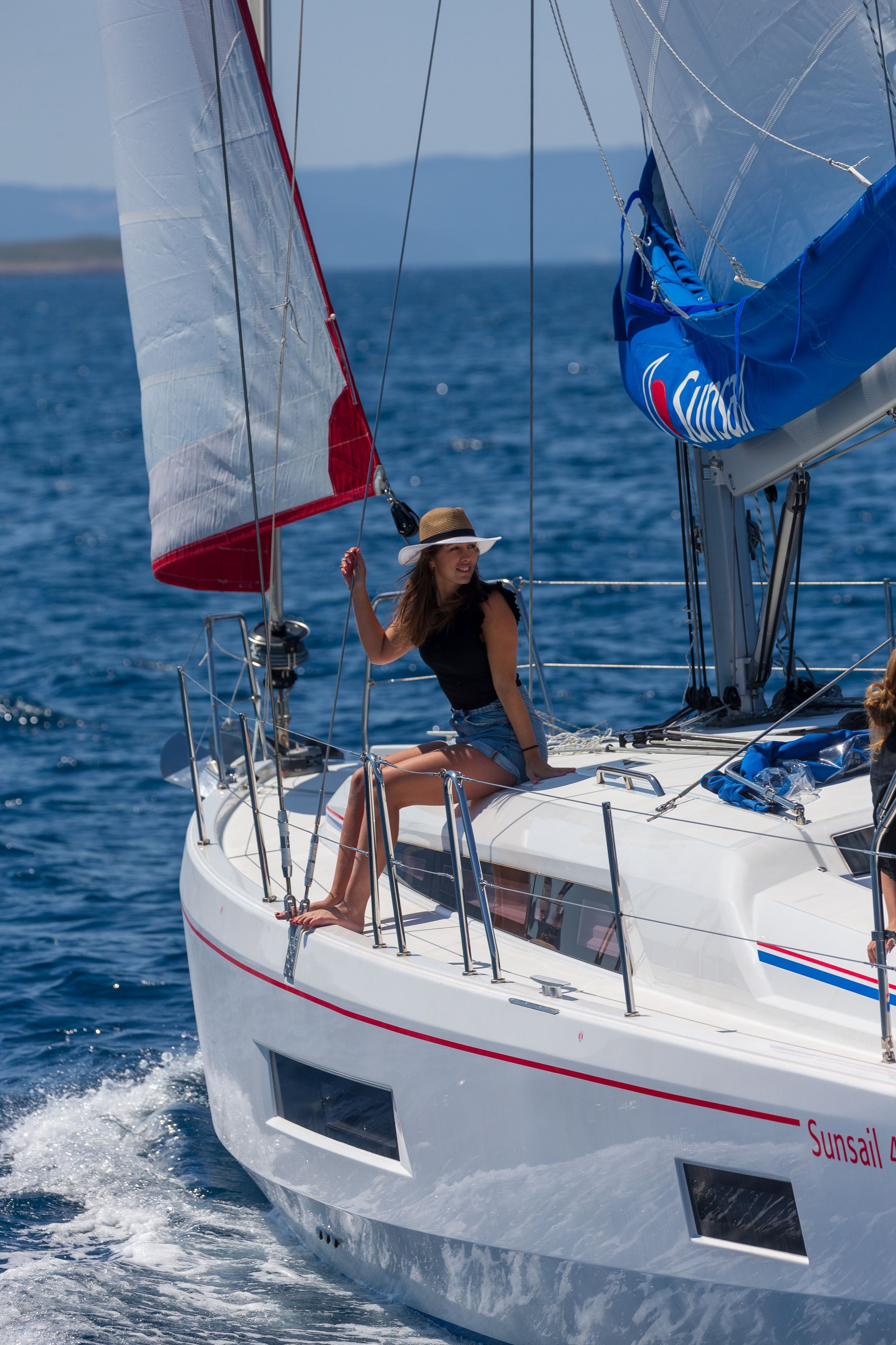Un voilier avec une personne sur le pont, une vue dégagée sur l’eau et le nom « Sunsail » inscrit sur le côté.