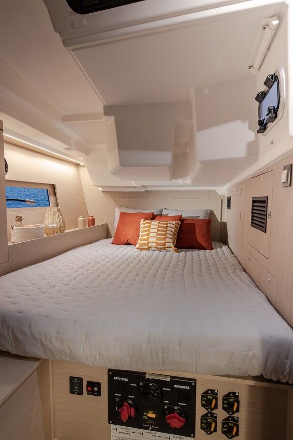 Una cama con un panel de control debajo, una ventana con vista al mar y un estante con objetos.
