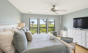 Ein Schlafzimmer mit Bett, Fernseher, Deckenventilator und Blick ins Freie.