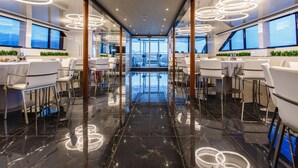 Ein modernes Hotelinterior mit einem zentralen, spiegelnden Boden, runden Deckenleuchten und großen Fenstern mit Ausblick.