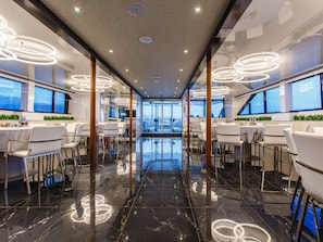 A modern hotel interior with a central reflective floor, circular ceiling lights, and large windows offering views.