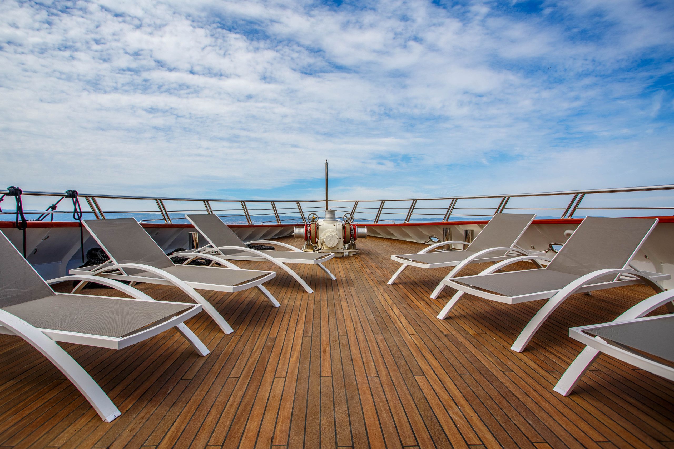 Een terras met ligbedden en een stuurwiel, met uitzicht op zee.