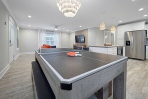 A modern kitchen with a ping pong table, stainless steel appliances, and a large window. - Costa Del Sol | Golf Cart~Beach Access~Games (Emerald Isle)