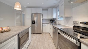 Une cuisine moderne avec des armoires blanches, des appareils en acier inoxydable et un plan de travail en bois.