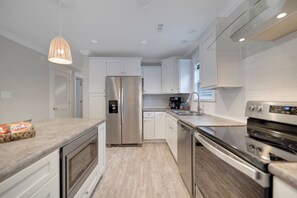 A modern kitchen with white cabinets, stainless steel appliances, and a wooden countertop. - Costa Del Sol | Golf Cart~Beach Access~Games (Emerald Isle)