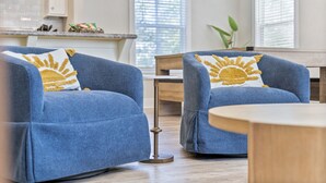 Une pièce avec deux fauteuils bleus, une table en bois et, au fond, une cuisine.