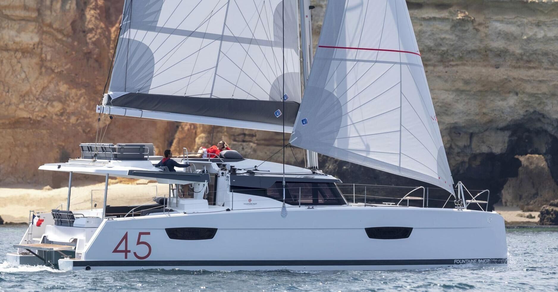 Un voilier portant le numéro 45 sur sa coque, naviguant près d’une côte rocheuse.