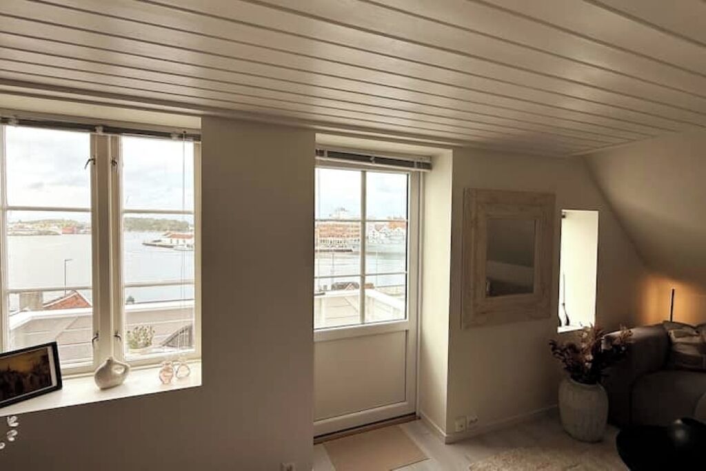 A room with large windows, a view of a body of water, a white ceiling, and a sofa.