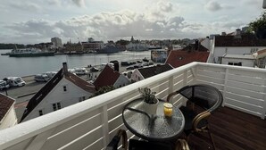 Een balkon met een tafel en stoelen, uitkijkend op een haven met boten en gebouwen.