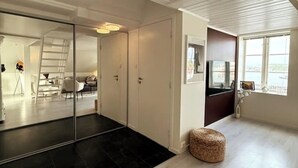 Een modern interieur met een glazen wand, een donkere vloer, een geweven poef en uitzicht door een raam.