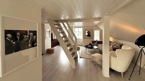 Een ruime loft met een houten trap, een gezellige zithoek en een grote foto in een lijst aan de muur.