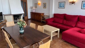 A dining area with a wooden table, chairs, a red sofa, and a fireplace. - Spacious 3-bedroom apartment on the front line by the sea. Rodes Lux-71 (Calafell)