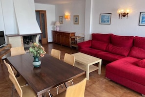 A dining area with a wooden table, chairs, a red sofa, and a fireplace. - Spacious 3-bedroom apartment on the front line by the sea. Rodes Lux-71 (Calafell)