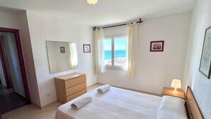 A hotel room with a bed, a dresser, a mirror, a window with curtains, and a nightstand with a lamp. - Spacious 3-bedroom apartment on the front line by the sea. Rodes Lux-71 (Calafell)