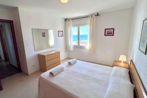 A hotel room with a bed, a dresser, a mirror, a window with curtains, and a nightstand with a lamp. - Spacious 3-bedroom apartment on the front line by the sea. Rodes Lux-71 (Calafell)