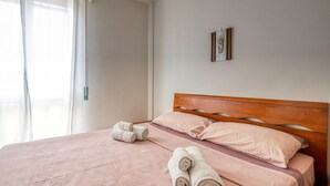 Un lit bien fait, avec du linge de lit rose et des serviettes pliées, une tête de lit en bois et un tableau encadré au mur.