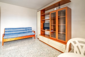 Une pièce avec un canapé en bois, un meuble avec des portes en verre et une chaise blanche.