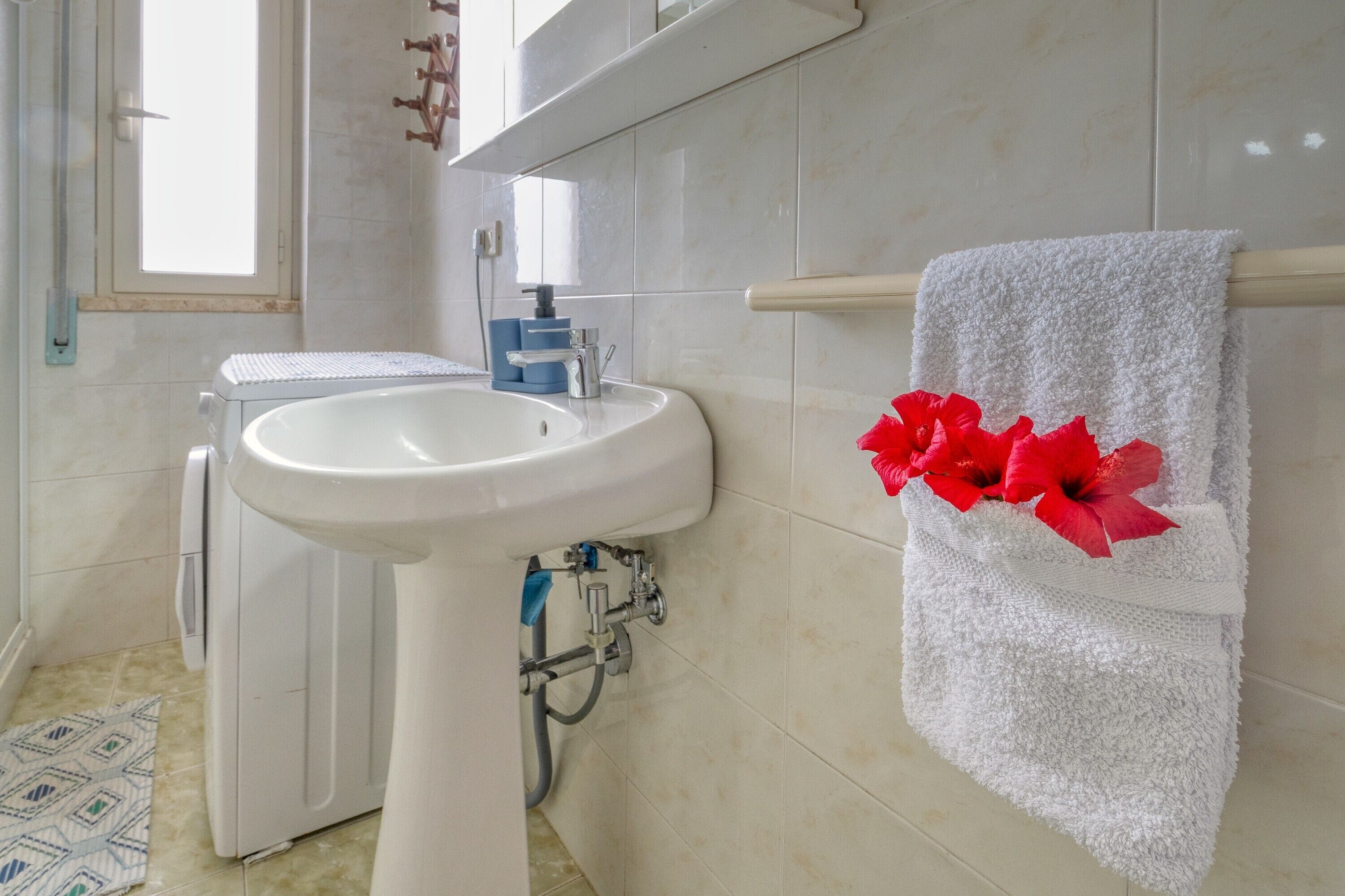 A bathroom with a white sink, a towel rack with a white towel, and a visible pipe.