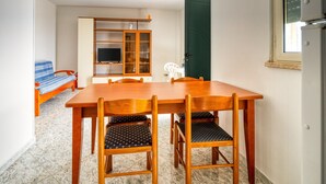 A compact room with a wooden dining table, two chairs, a television on a stand, and a sofa with a blue blanket. - Residence do Mestru Luccio Apt. Tripoli (San Pietro In Bevagna)