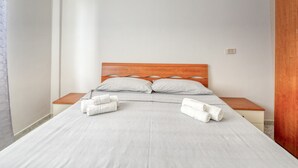 A neatly made bed with pillows and rolled towels, a wooden headboard, and a small bedside table. - Residence do Mestru Luccio Apt. Tripoli (San Pietro In Bevagna)