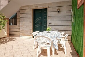 Eine Terrasse mit Tisch und Stühlen, eine grüne Tür und ein kleines Pflänzchen.